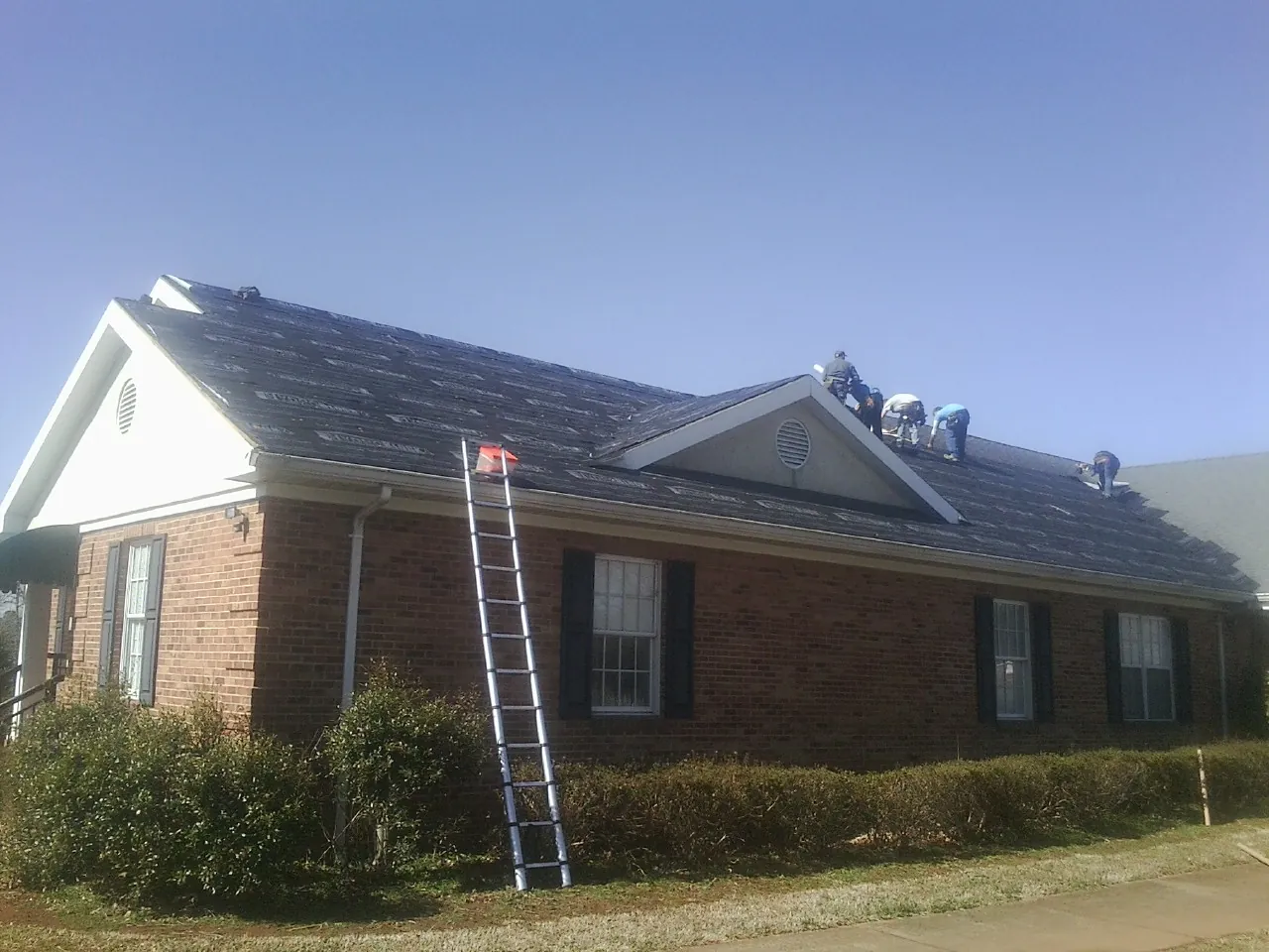 Crew tearing shingles off a brick ranch roof with a ladder set — Emergency Roof Repair work by our crew in Dunn