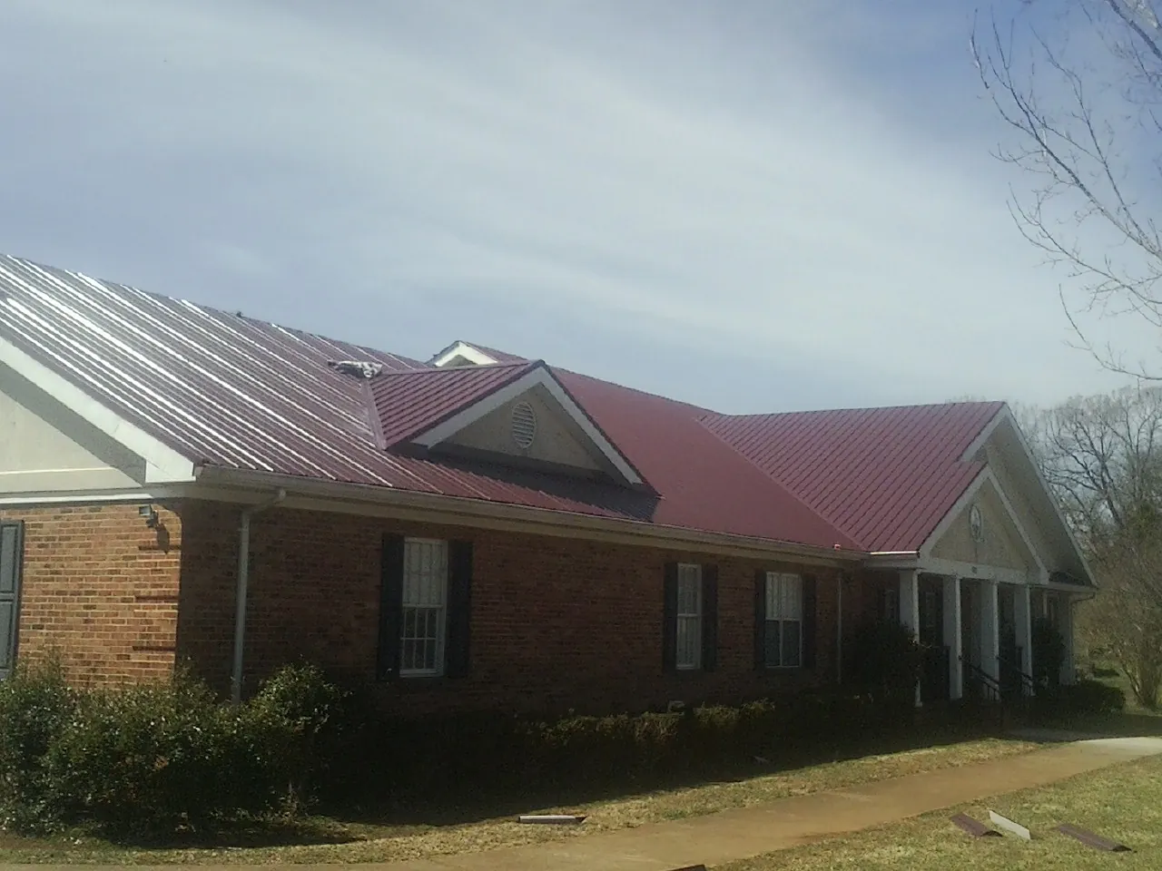 Red metal roof with gabled entries on a long brick building, from a Hail Damage Roof Repair job in Dunn