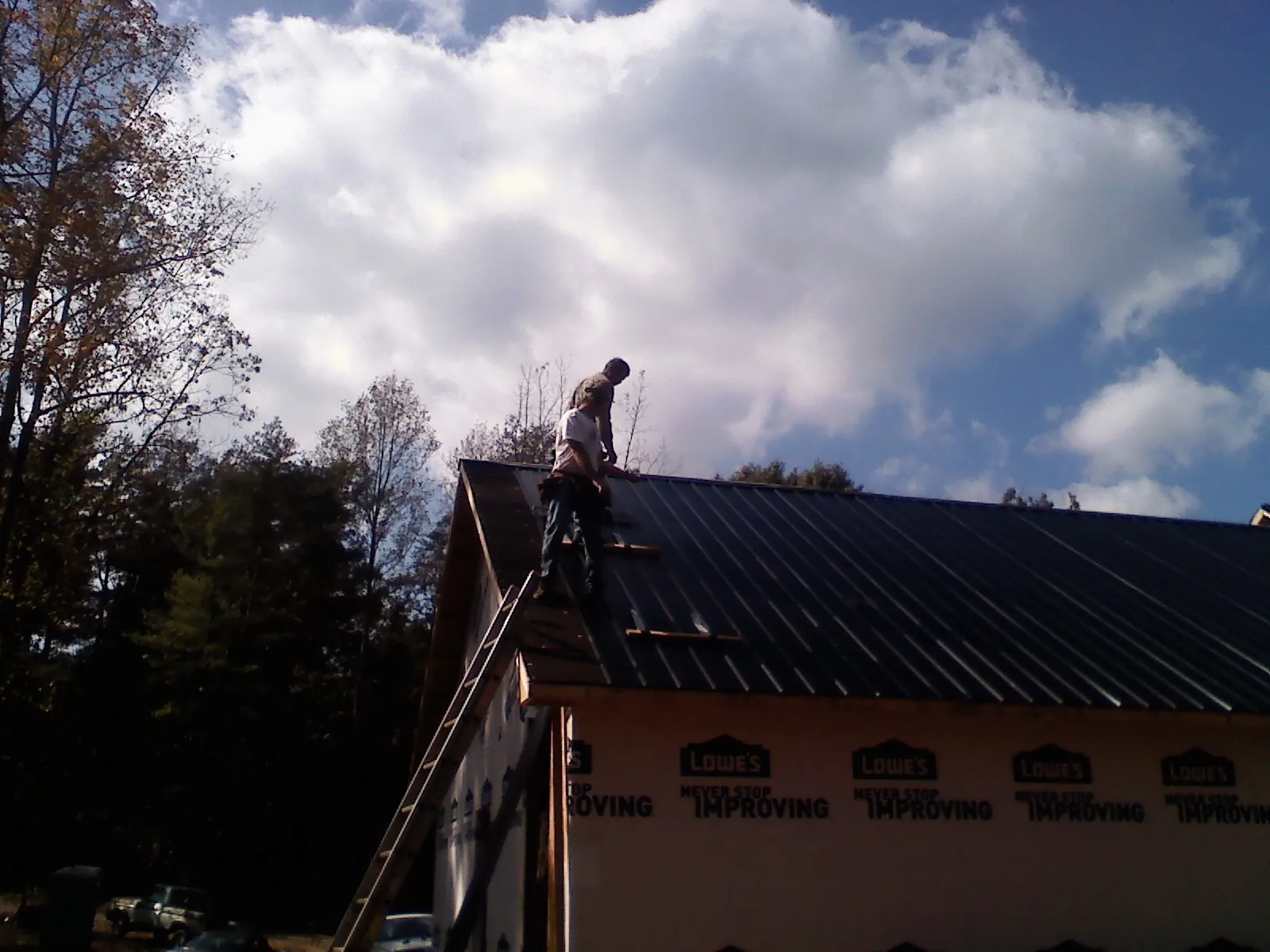 Roofer fastening dark metal panels high against a cloudy sky, from a Roof Inspection job in Dunn
