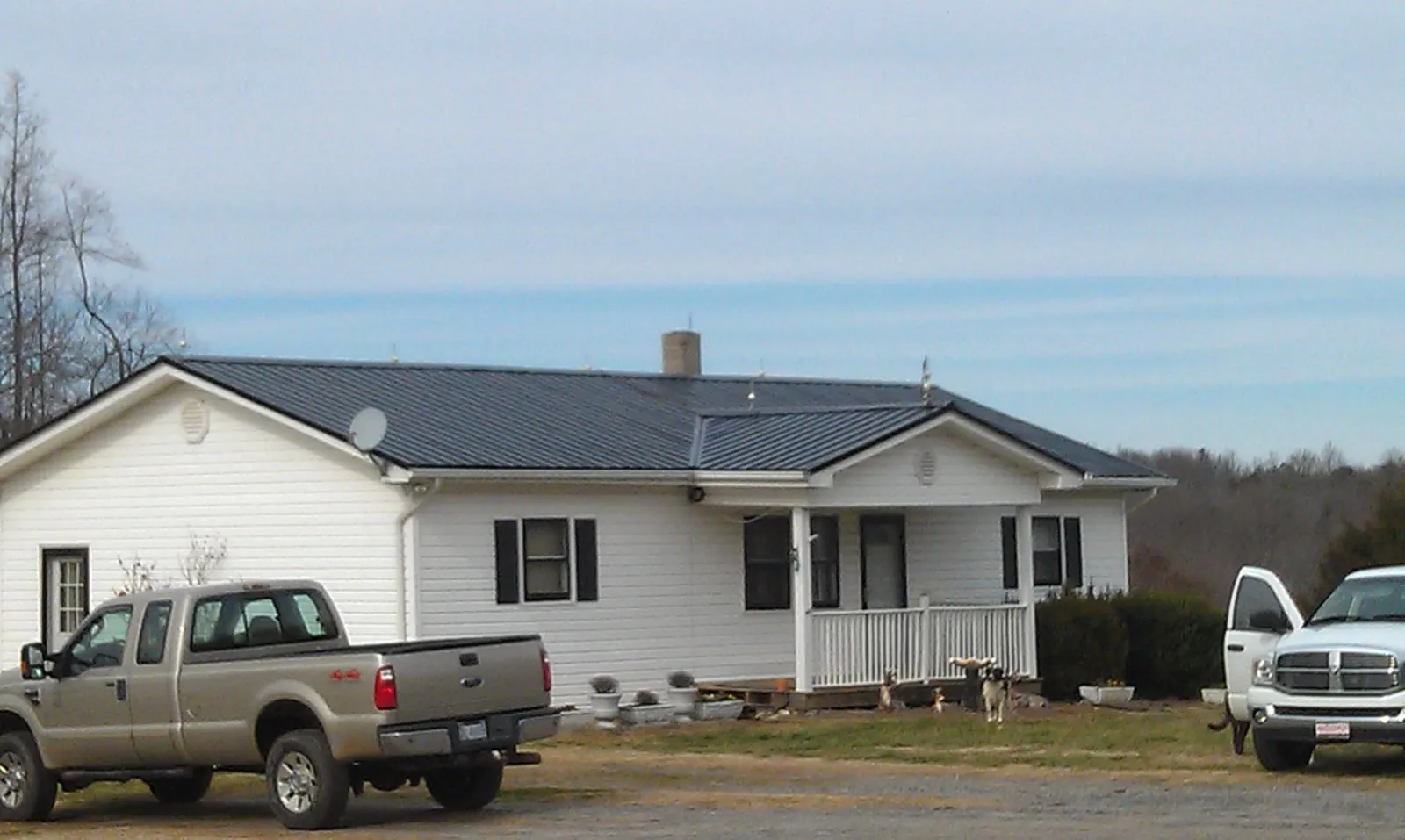 Finished dark metal roof on a white ranch home with work trucks parked in Dunn