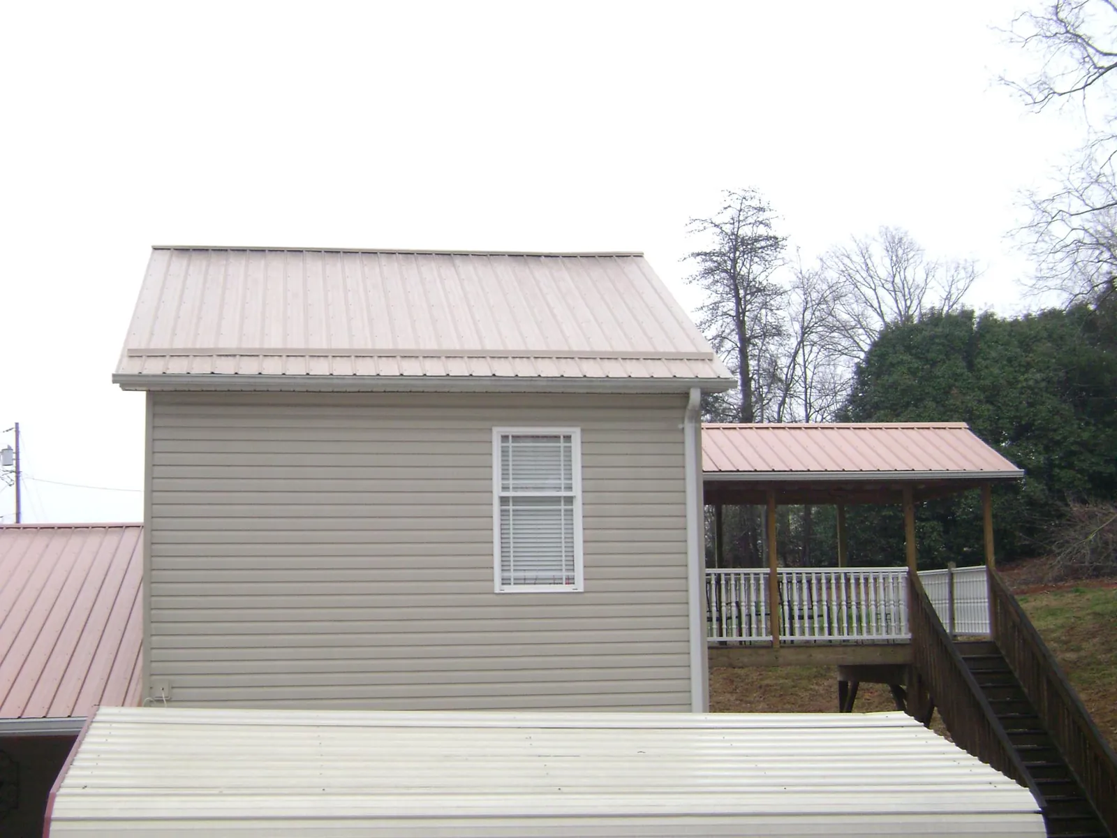 Tan metal roofs on a two story addition and attached porch, from a Roof Replacement job in Dunn